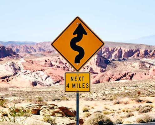 road sign in desert with curvy road warning